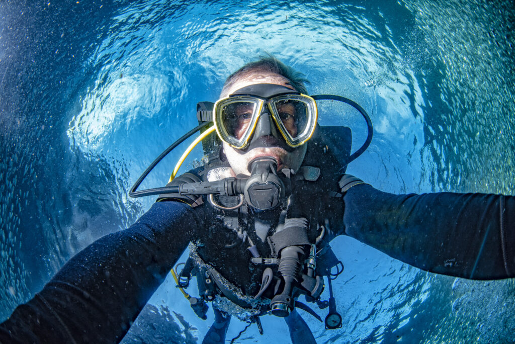 Scuba diver underwater selfie in the deep blue ocean and backlight sun and sardines bait ball